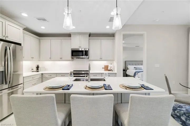 Kitchen featuring appliances with stainless steel finishes, a breakfast bar area, an island with sink, recessed lighting, and decorative light fixtures
