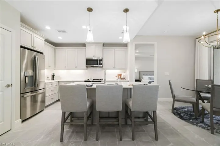 Kitchen featuring stainless steel appliances, a kitchen breakfast bar, a center island with sink, white cabinets, and recessed lighting