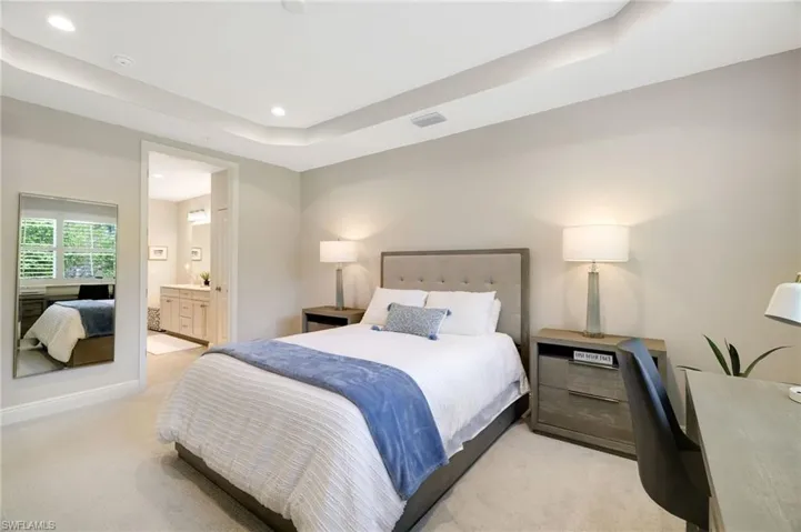 Bedroom with a raised ceiling, ensuite bathroom, light carpet, and recessed lighting