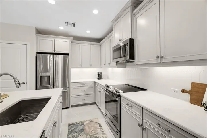Kitchen with appliances with stainless steel finishes, light stone countertops, recessed lighting, and white cabinets