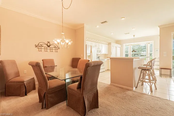 Dining room with ornamental molding, light carpet, and an inviting chandelier