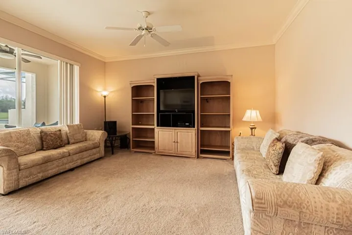 Carpeted living room featuring ceiling fan and ornamental molding