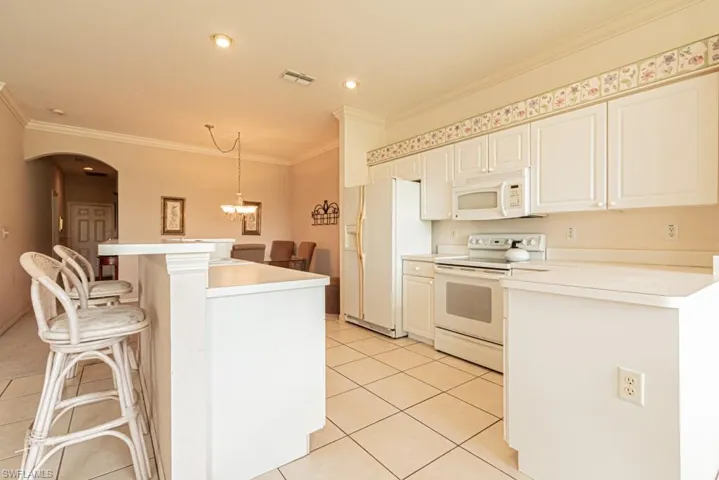 Kitchen featuring white appliances, light tile patterned floors, ornamental molding, decorative light fixtures, and a breakfast bar area
