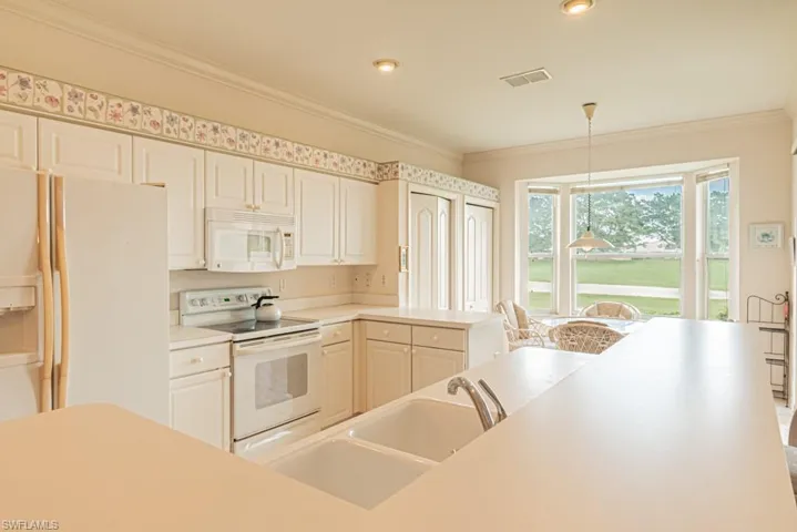 Kitchen with white appliances, decorative light fixtures, crown molding, and sink