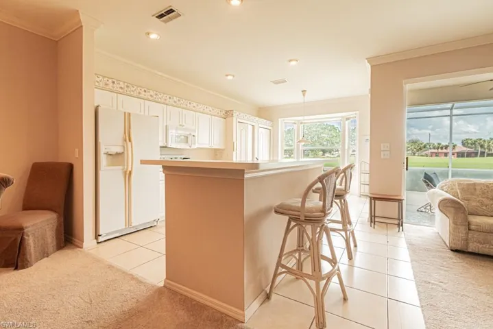 Kitchen featuring pendant lighting, white appliances, light tile patterned floors, ornamental molding, and a breakfast bar area