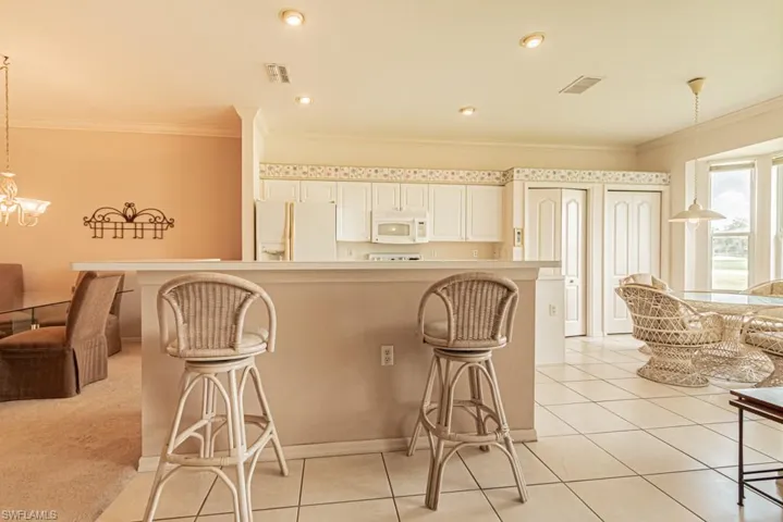 Kitchen featuring pendant lighting, a breakfast bar, white appliances, and ornamental molding