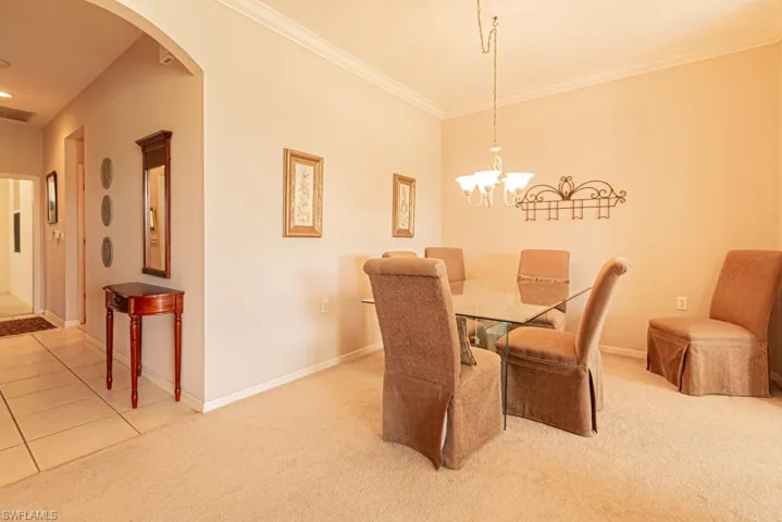 Carpeted dining space with a notable chandelier and crown molding