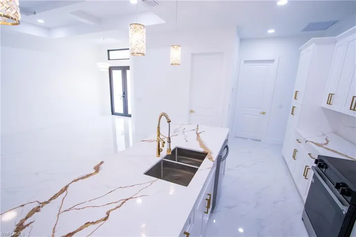 Kitchen with white cabinetry, sink, hanging light fixtures, and range with electric cooktop
