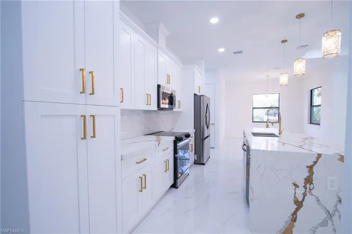Kitchen featuring sink, light stone counters, hanging light fixtures, appliances with stainless steel finishes, and white cabinets