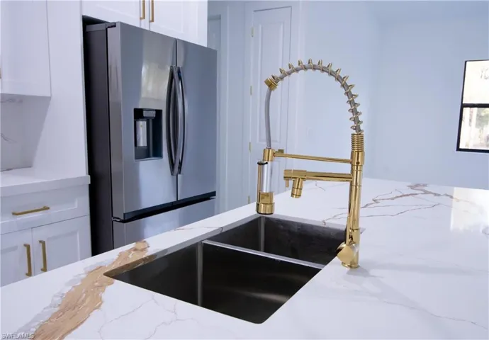 Kitchen with light stone counters, white cabinetry, and stainless steel fridge with ice dispenser