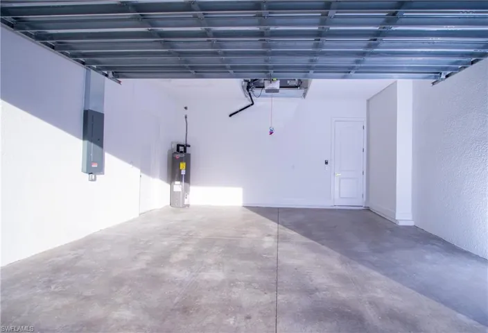Garage with a garage door opener, electric panel, and electric water heater