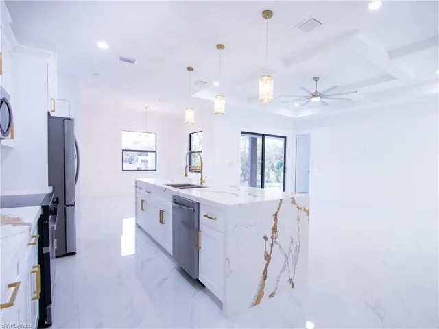 Kitchen featuring appliances with stainless steel finishes, decorative light fixtures, white cabinets, a kitchen island with sink, and light stone countertops