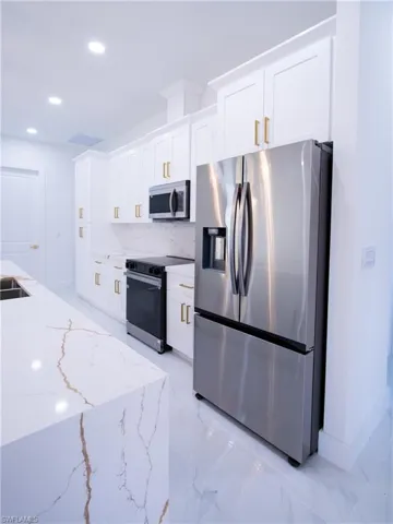 Kitchen featuring light stone counters, sink, white cabinetry, and stainless steel appliances