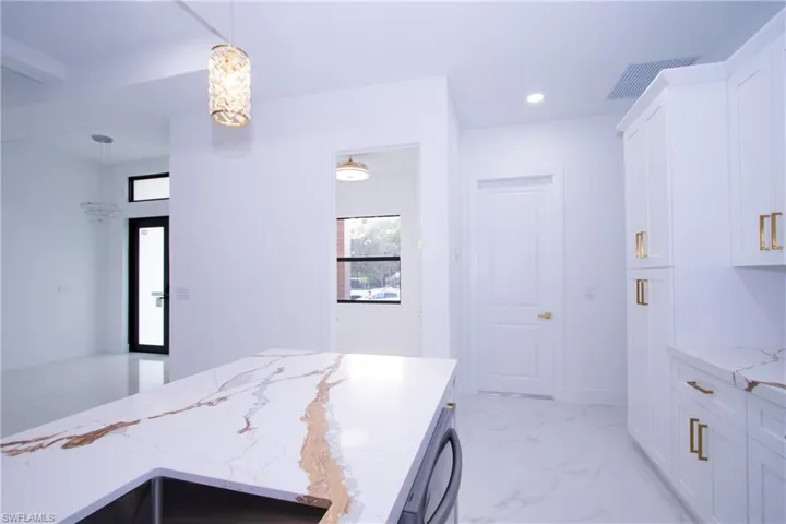 Kitchen featuring light stone counters, decorative light fixtures, dishwasher, and white cabinets