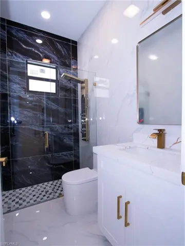 Bathroom with vanity, a shower with shower door, toilet, and tile walls