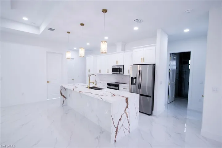 Kitchen featuring decorative light fixtures, white cabinetry, sink, light stone counters, and stainless steel appliances