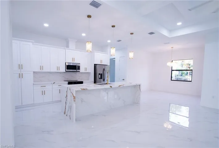 Kitchen with white cabinetry, light stone countertops, pendant lighting, and stainless steel appliances
