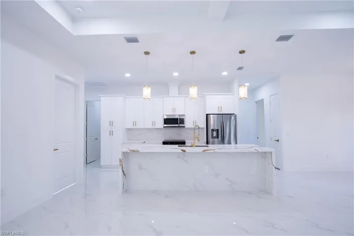 Kitchen with stainless steel appliances, white cabinetry, pendant lighting, and light stone counters
