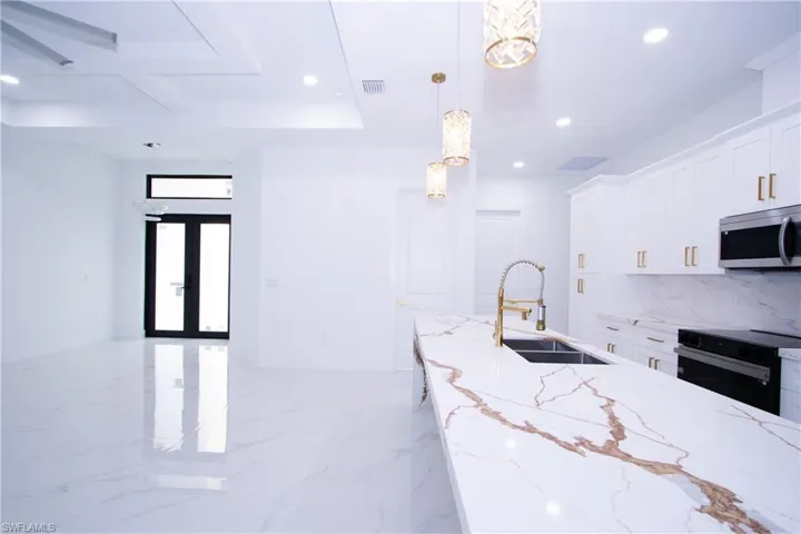 Kitchen with decorative light fixtures, white cabinetry, sink, oven, and light stone countertops