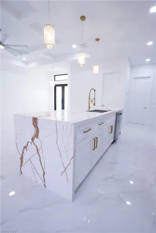 Kitchen featuring sink, white cabinetry, dishwasher, pendant lighting, and light stone countertops