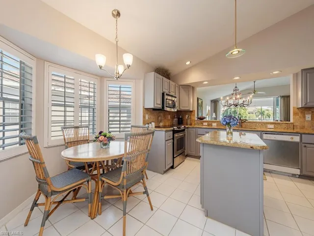 Kitchen featuring gray cabinetry, a chandelier, vaulted ceiling, stainless steel appliances, and light stone countertops