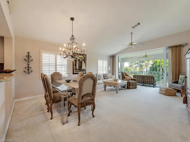 Dining area featuring light carpet, ceiling fan, vaulted ceiling, and a chandelier