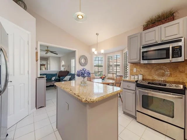Kitchen featuring gray cabinets, appliances with stainless steel finishes, vaulted ceiling, a center island, and decorative light fixtures