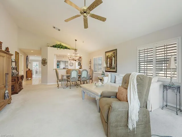 Carpeted living area with high vaulted ceiling, ceiling fan, and a chandelier