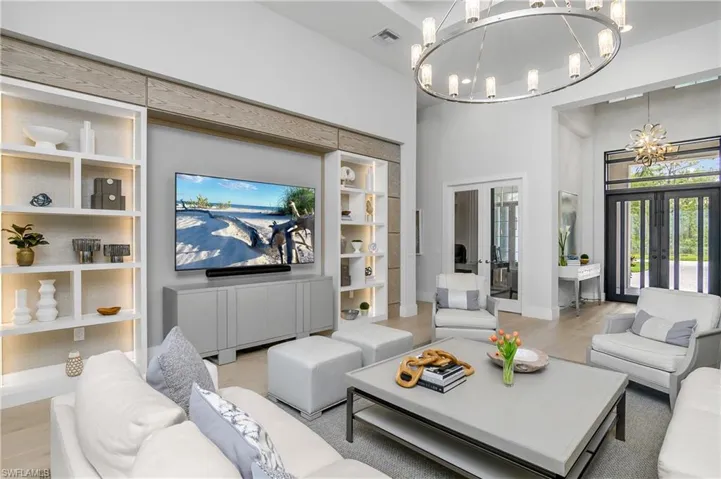 Living room with a high ceiling, light wood-type flooring, french doors, and an inviting chandelier
