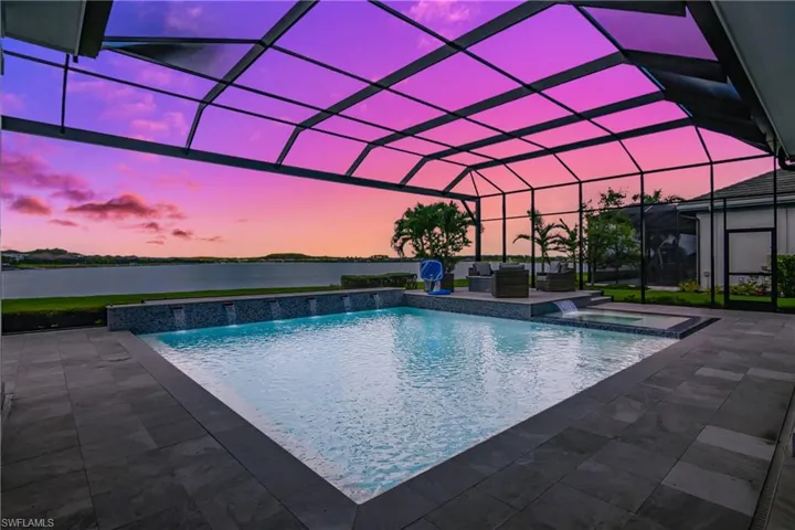 Pool at dusk with an in ground hot tub, a patio, glass enclosure, and a water view