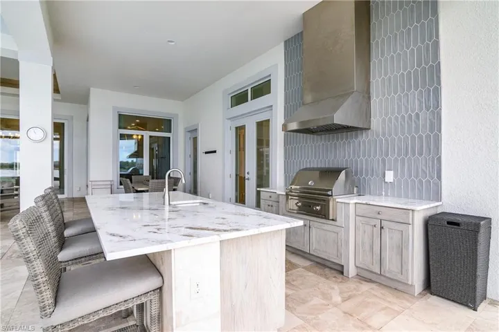 Kitchen with light stone countertops, light brown cabinets, wall chimney exhaust hood, sink, and a kitchen bar