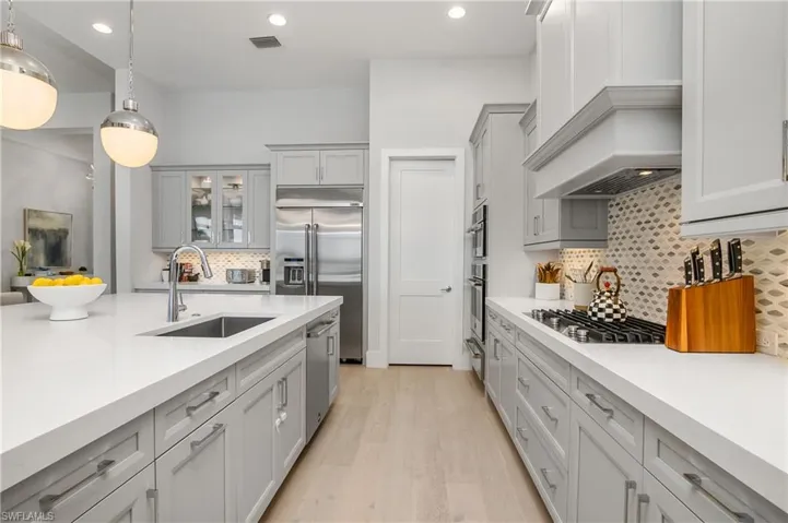 Kitchen featuring custom range hood, sink, light hardwood / wood-style floors, pendant lighting, and appliances with stainless steel finishes