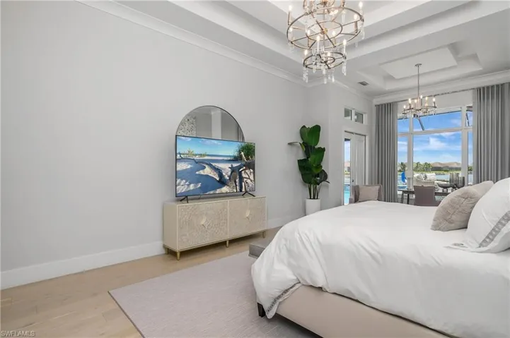Bedroom featuring wood-type flooring, an inviting chandelier, a raised ceiling, and ornamental molding