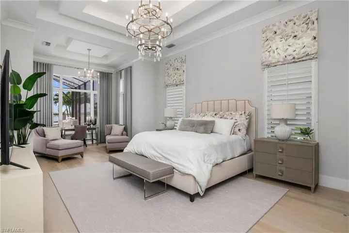 Bedroom featuring a raised ceiling, an inviting chandelier, crown molding, and light hardwood / wood-style flooring