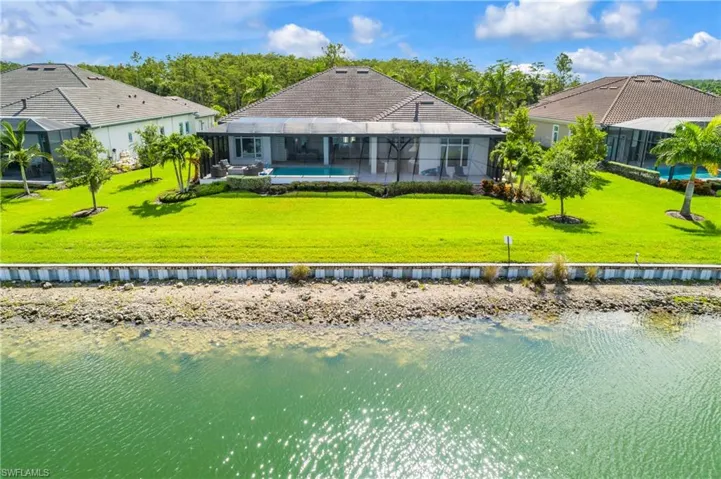 Back of house with a lanai, a lawn, and a water view