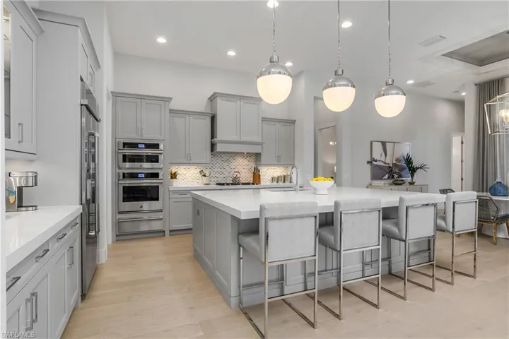 Kitchen with a breakfast bar area, stainless steel appliances, hanging light fixtures, and gray cabinetry