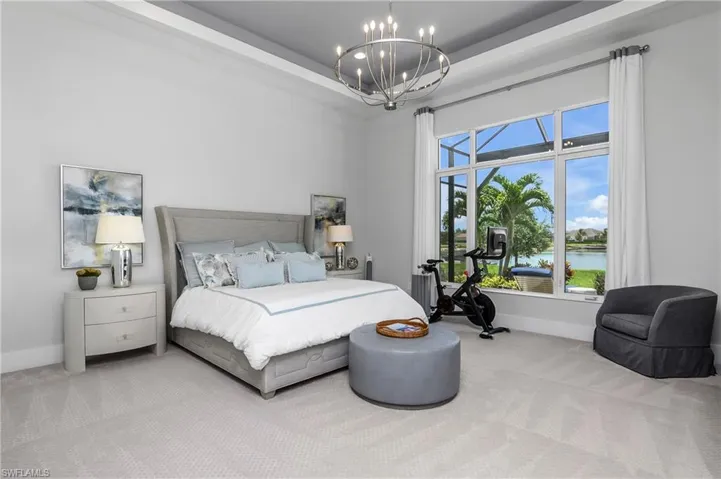 Carpeted bedroom featuring a water view, a raised ceiling, and a notable chandelier