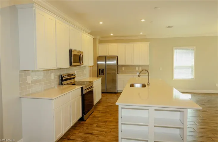 Kitchen with stainless steel appliances, white cabinetry, an island with sink, dark wood finished floors, and crown molding