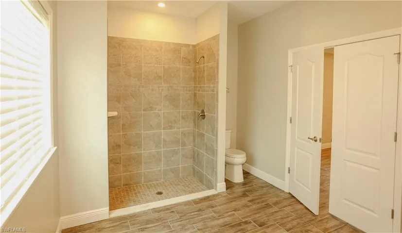Bathroom featuring tiled shower, wood finish floors, and plenty of natural light