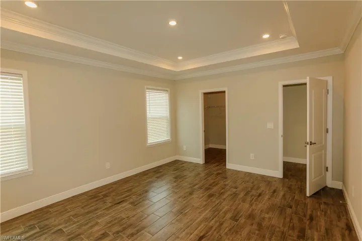 Unfurnished bedroom with a spacious closet, recessed lighting, wood tiled floors, crown molding, and a raised ceiling