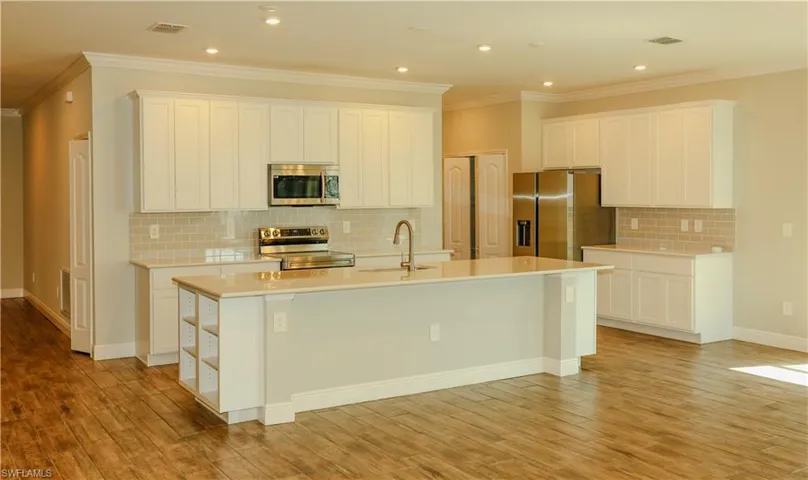 Kitchen featuring an island with sink, white cabinetry, stainless steel appliances, ornamental molding, and decorative backsplash