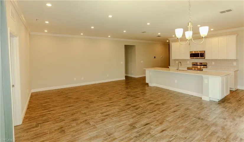 Kitchen with an island with sink, white cabinets, stainless steel appliances, light wood-type flooring, and ornamental molding