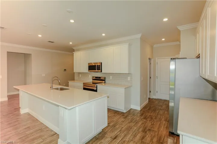 Kitchen with white cabinetry, stainless steel appliances, light wood-style flooring, a center island with sink, and recessed lighting