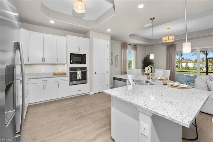 Kitchen featuring a tray ceiling, appliances with stainless steel finishes, wood tiled floors, white cabinetry, and a spacious island
