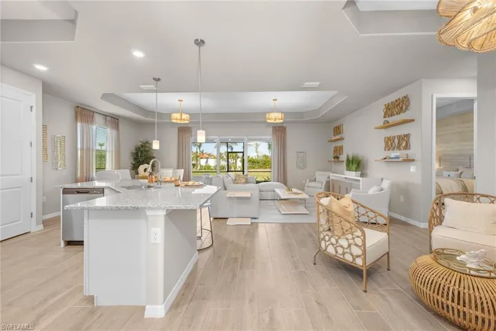 Kitchen featuring a raised ceiling, healthy amount of natural light, an island with sink, light stone counters, and recessed lighting