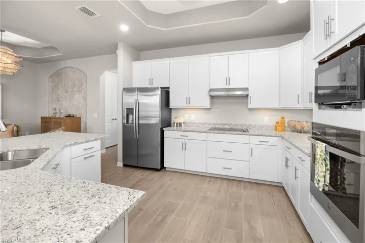 Kitchen featuring a raised ceiling, black appliances, recessed lighting, white cabinets, and light wood-style floors