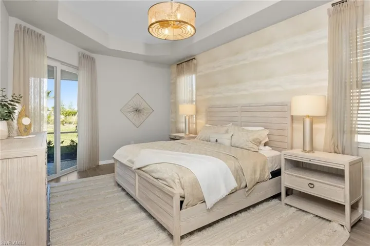 Bedroom with a tray ceiling, access to exterior, wood finished floors, and a chandelier