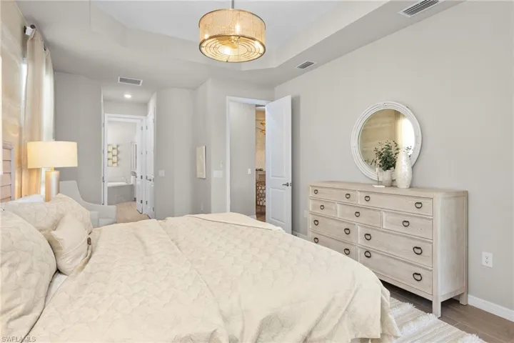 Bedroom featuring a tray ceiling, light wood-type flooring, and ensuite bath