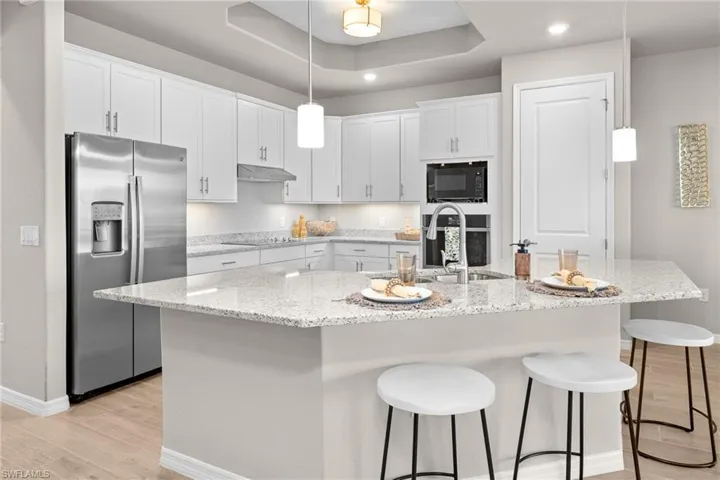 Kitchen featuring black appliances, white cabinets, light wood finished floors, a kitchen bar, and recessed lighting