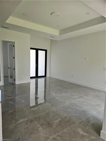 Tiled spare room featuring a tray ceiling and french doors